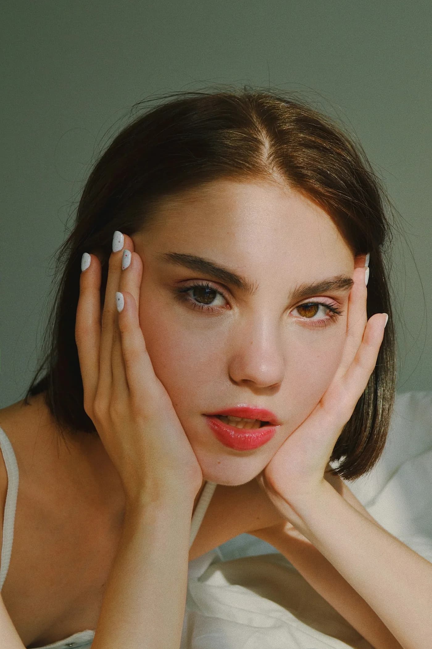 Woman in white resting her face in her hands, pale manicured nails
