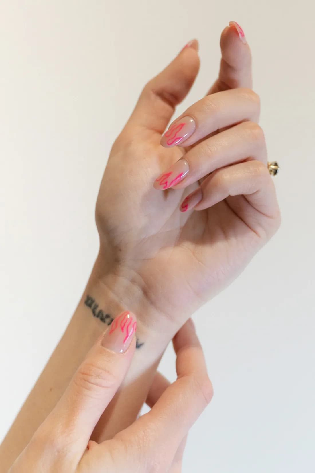Hands with soft pink nails raised against a cream wall