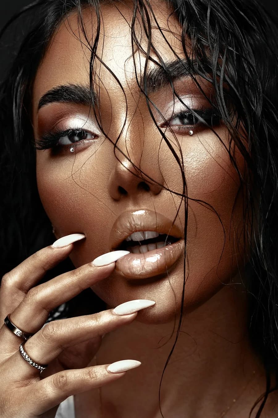 Woman with wet-look hair and long white nails at her lips