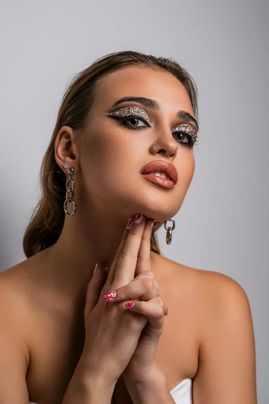 Woman with rhinestone eye make-up, red patterned nails at her chin