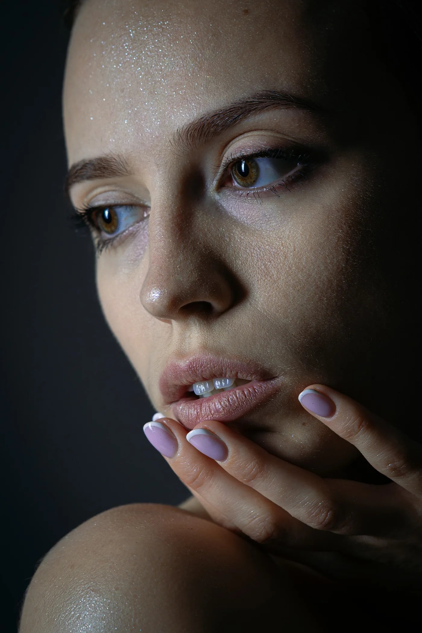 Close portrait of a woman with pale lilac nails touching her lips
