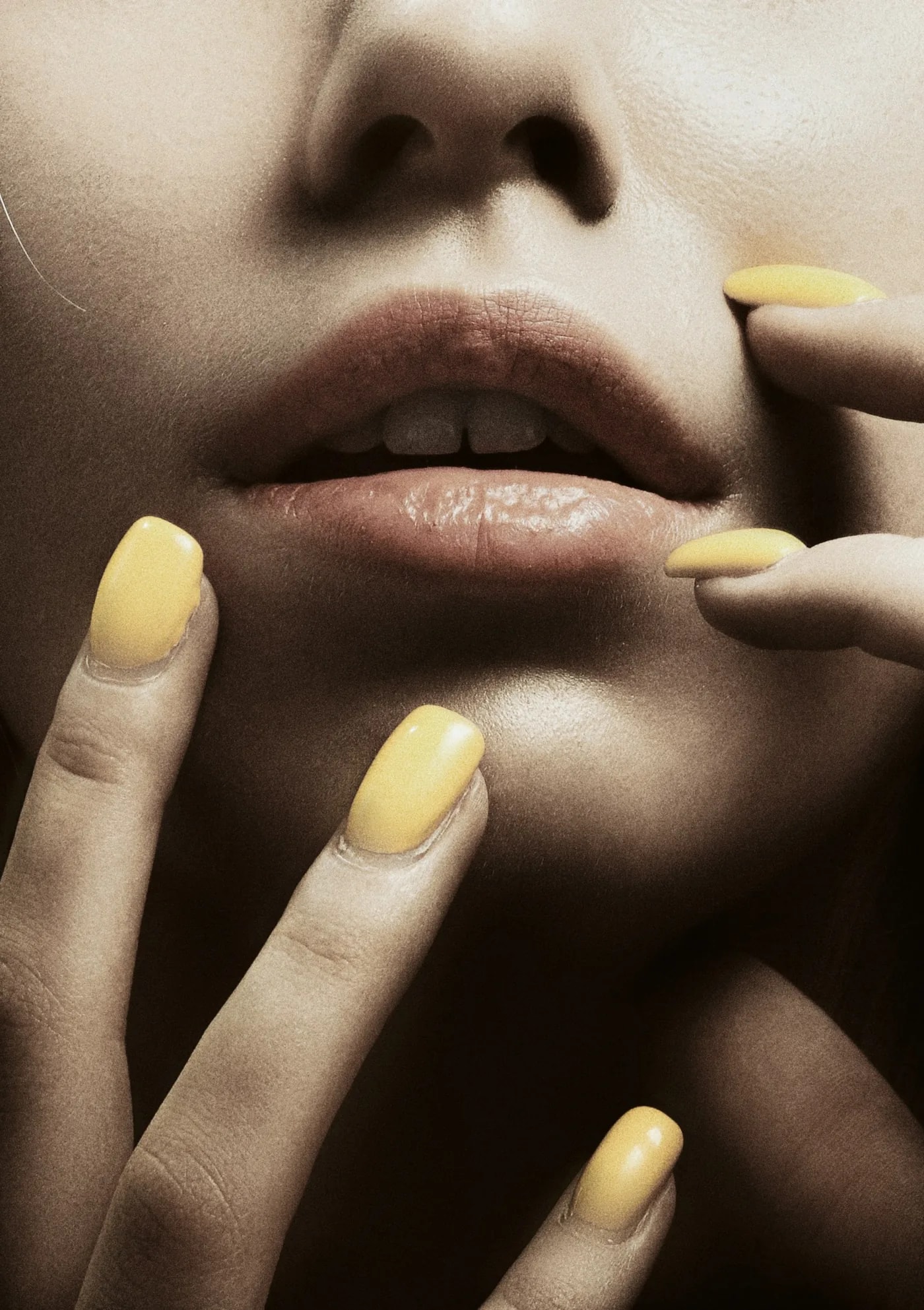 Close-up of lips with soft yellow nails resting on them