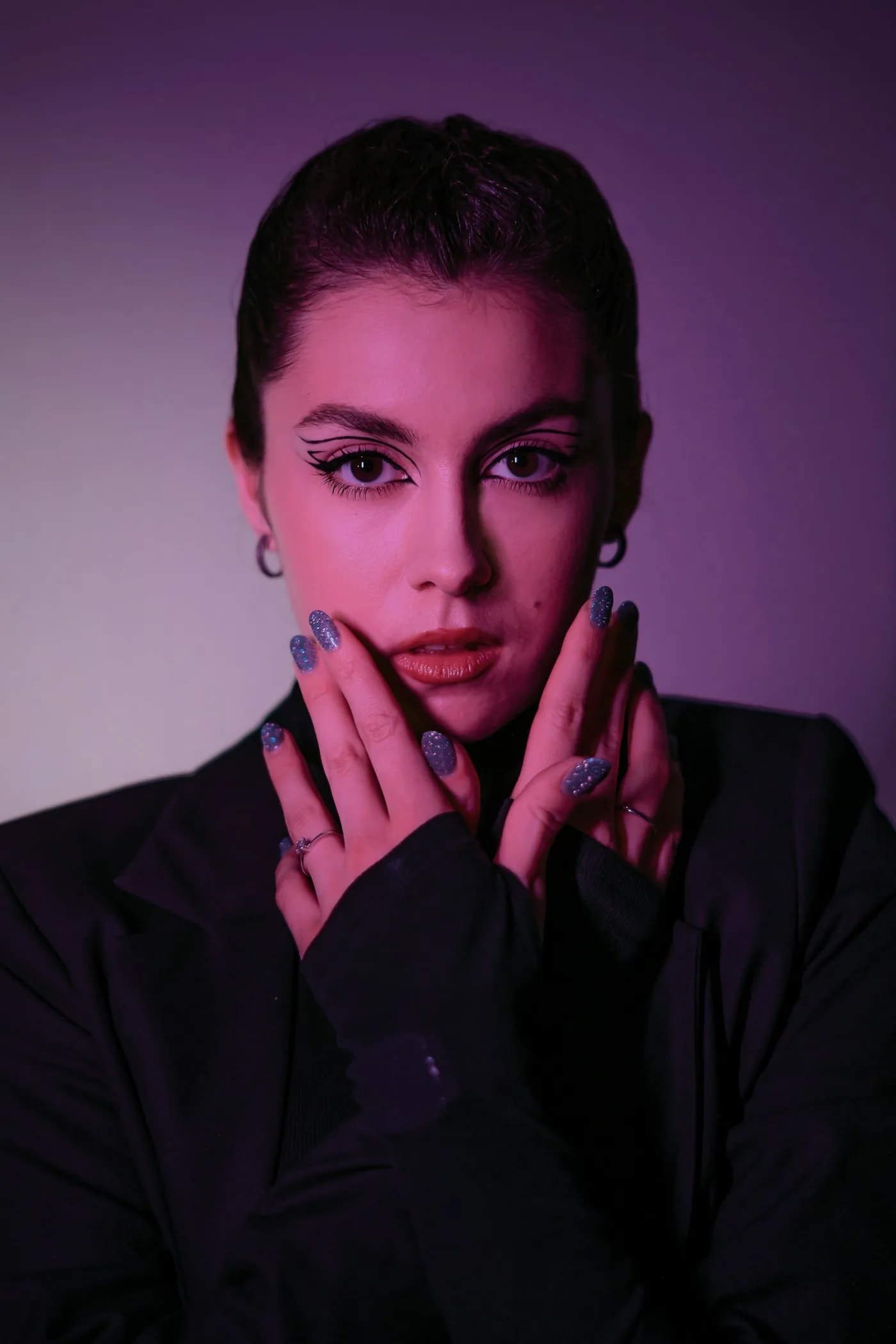 Woman in violet light framing her face with her hands