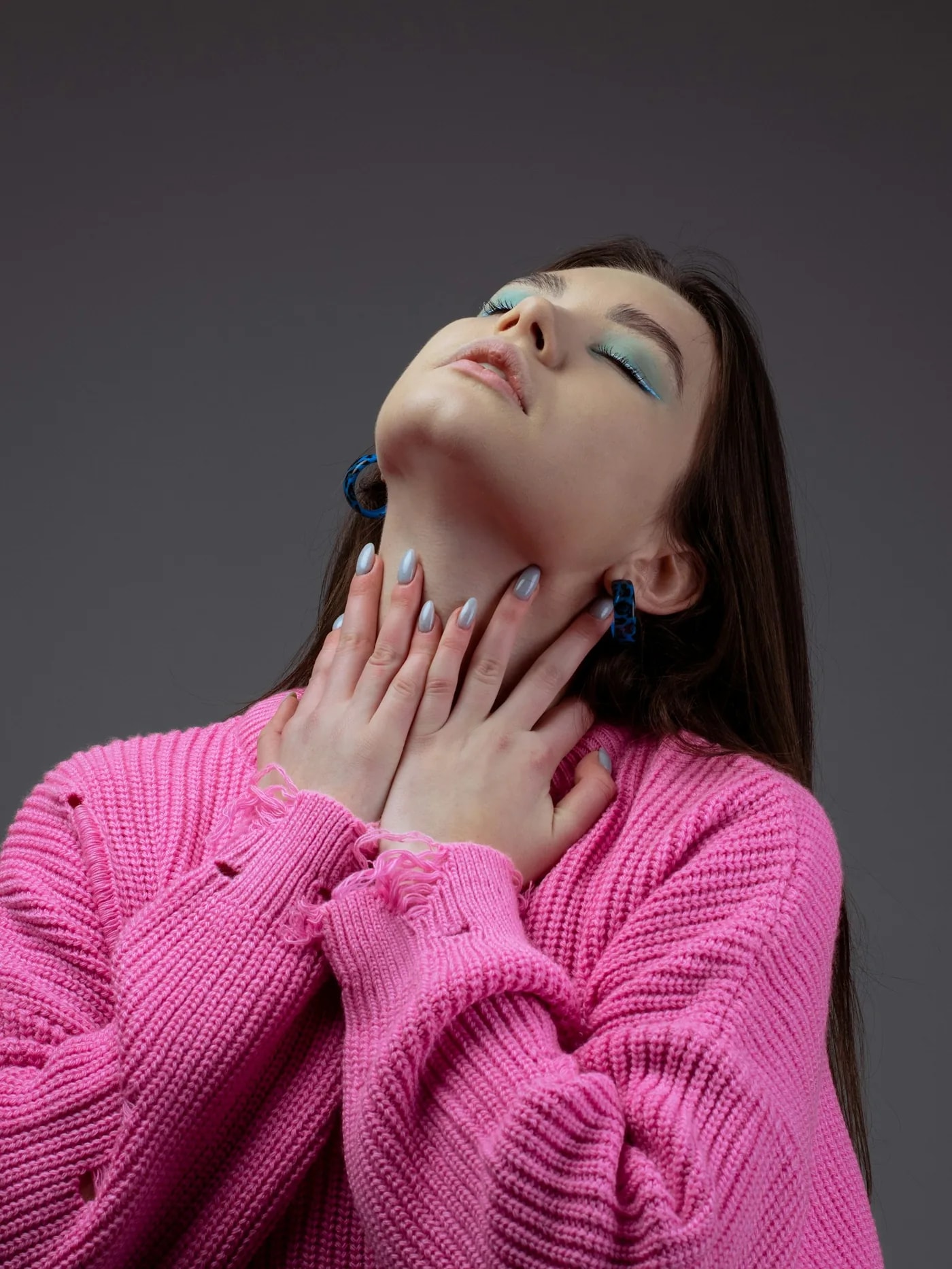 Woman in a pink knit with her head tilted back, hands at her neck