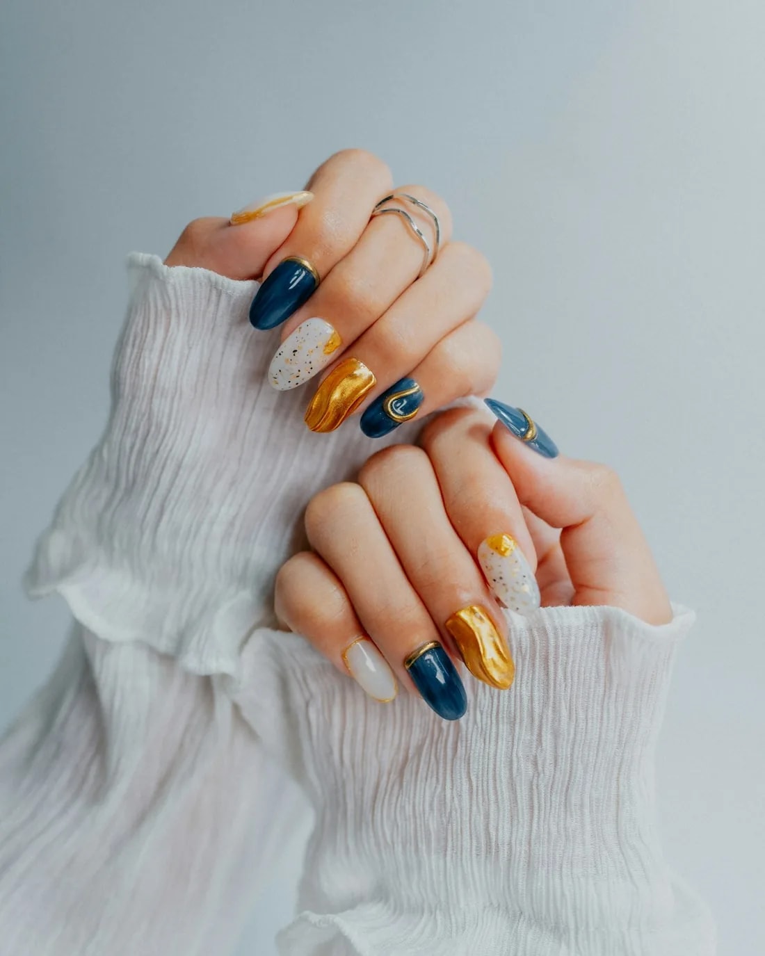 Hands with navy and gold nails in white ruffled sleeves