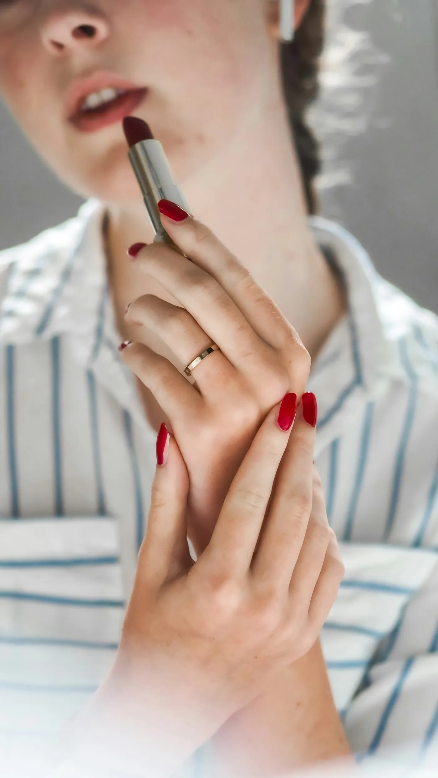 Woman in a striped shirt applying lipstick, red nails
