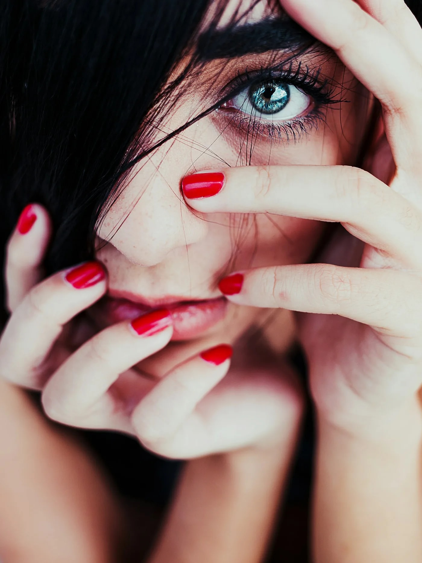 Woman with a blue eye looking through hands with red nails