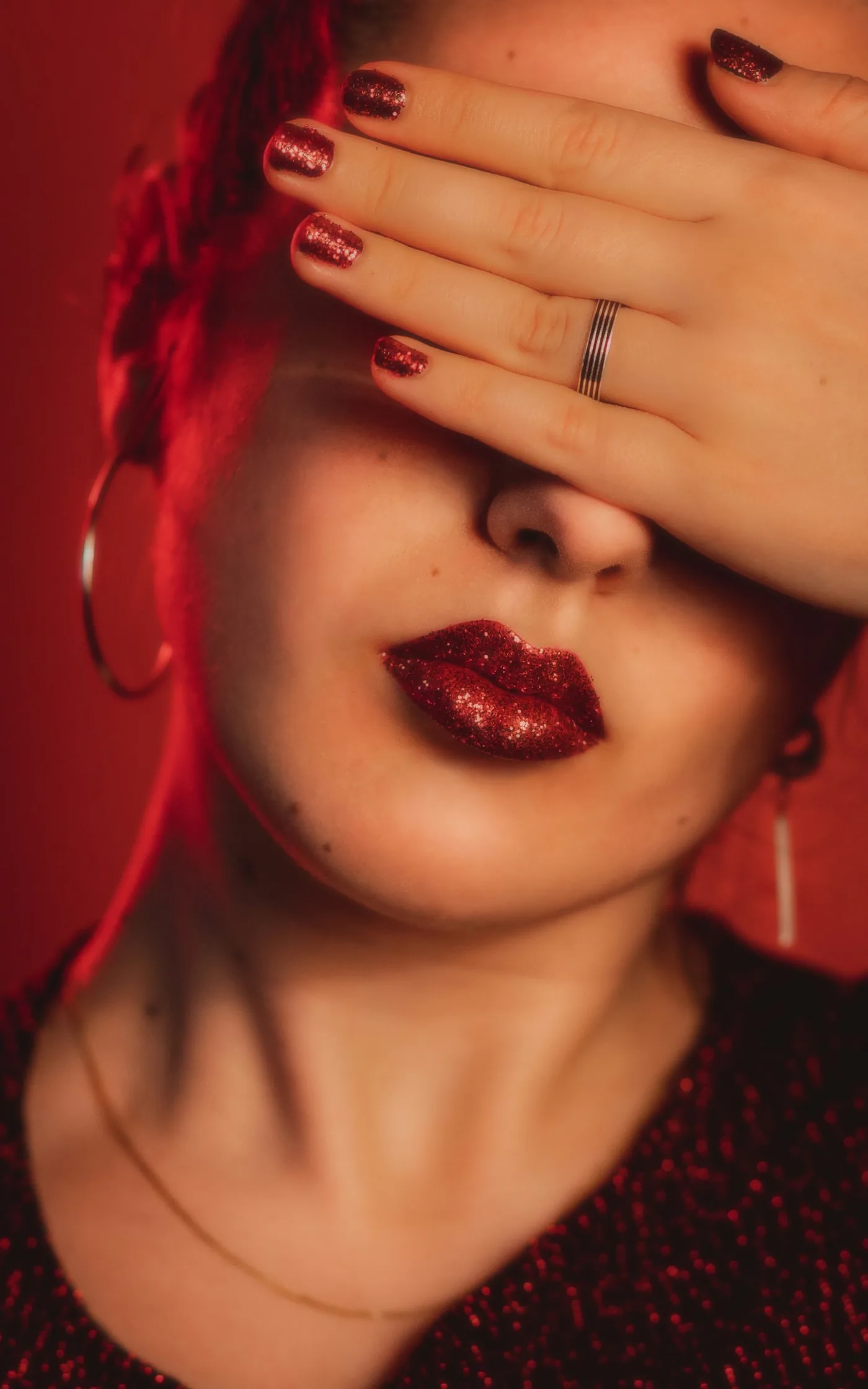 Woman covering her eyes with her hand, deep burgundy nails and glitter lips